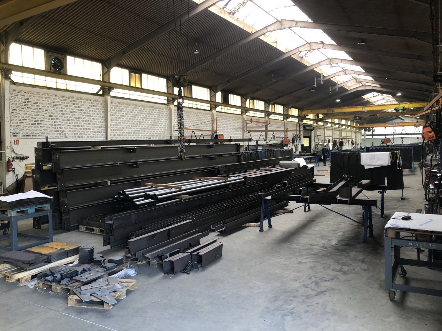 Werkshalle mit Fahrzeugkran, mehreren Stahlrahmen und Metallkomponenten, bereit zur Montage.